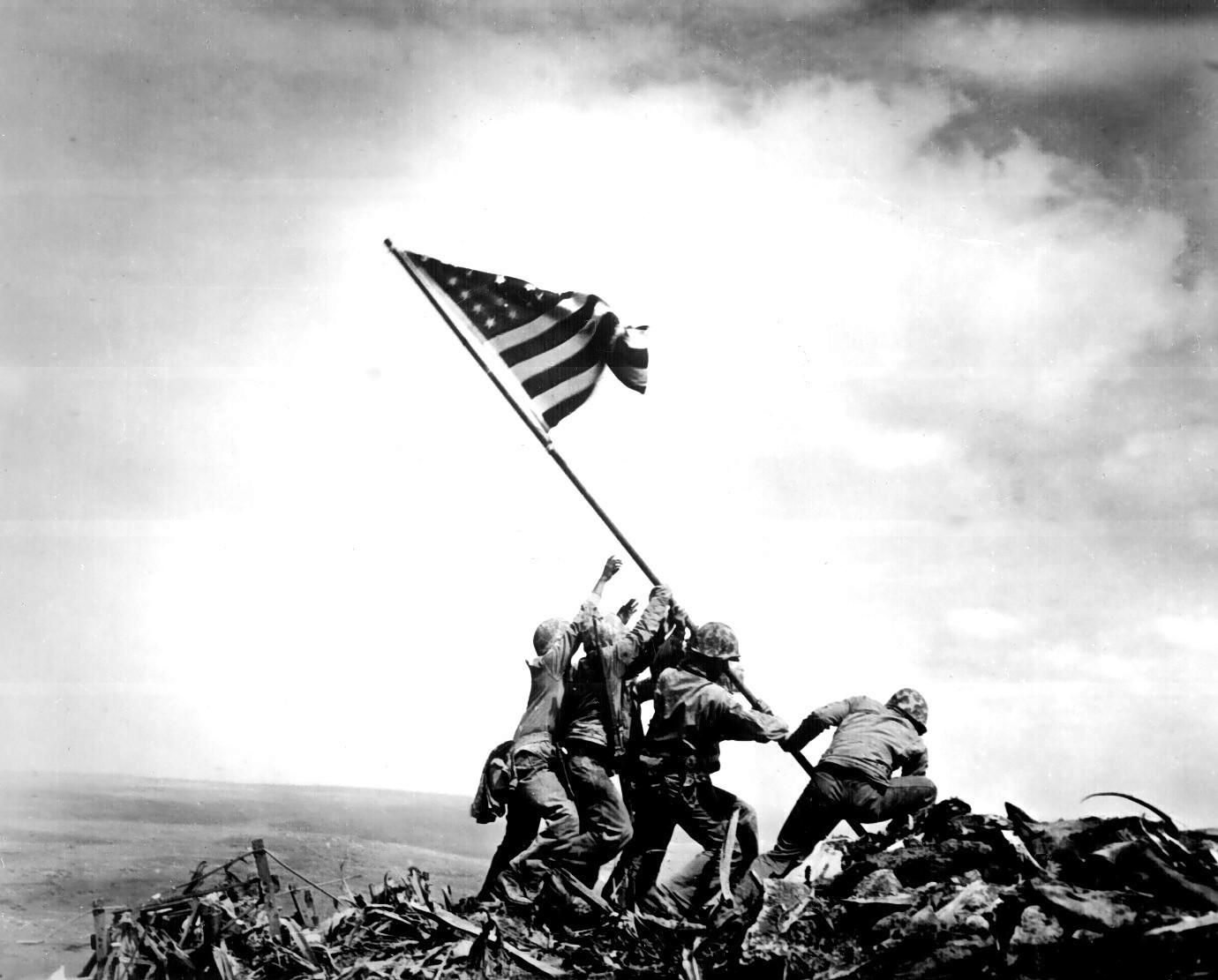 soldados andando sobre uma pilha de destroços, carregando uma haste com a bandeira americana